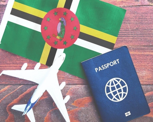 Dominica flag, a small model airplane, and a passport arranged on a wooden surface.