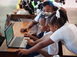 Children in school uniforms gathered around a laptop, engaging in a classroom activity.